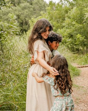 A tender embrace shared between people walking together on a dirt path surrounded by lush greenery on a sunny day.