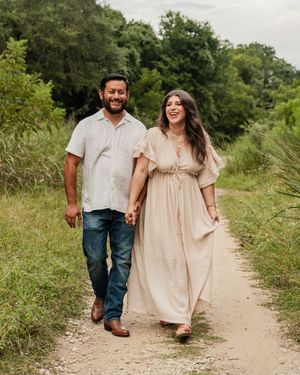 A couple walking together on a dirt path through lush green foliage wearing casual clothing.