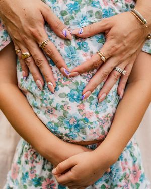 Close up view of hands resting on a floral patterned dress or fabric showing multiple gold rings and blue nail polish.