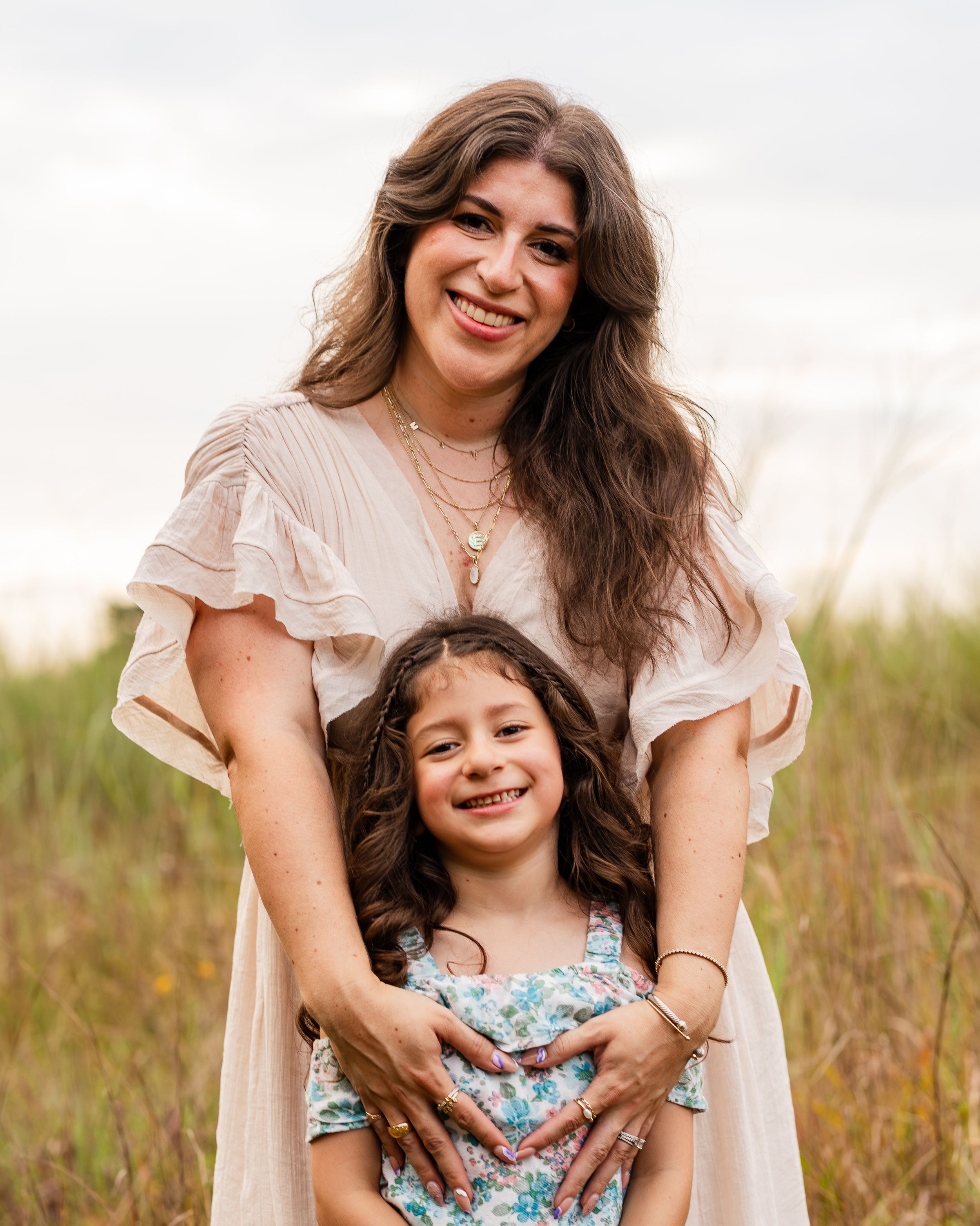 A touching family portrait shows a mother and daughter embracing in a field of tall grass at sunset.