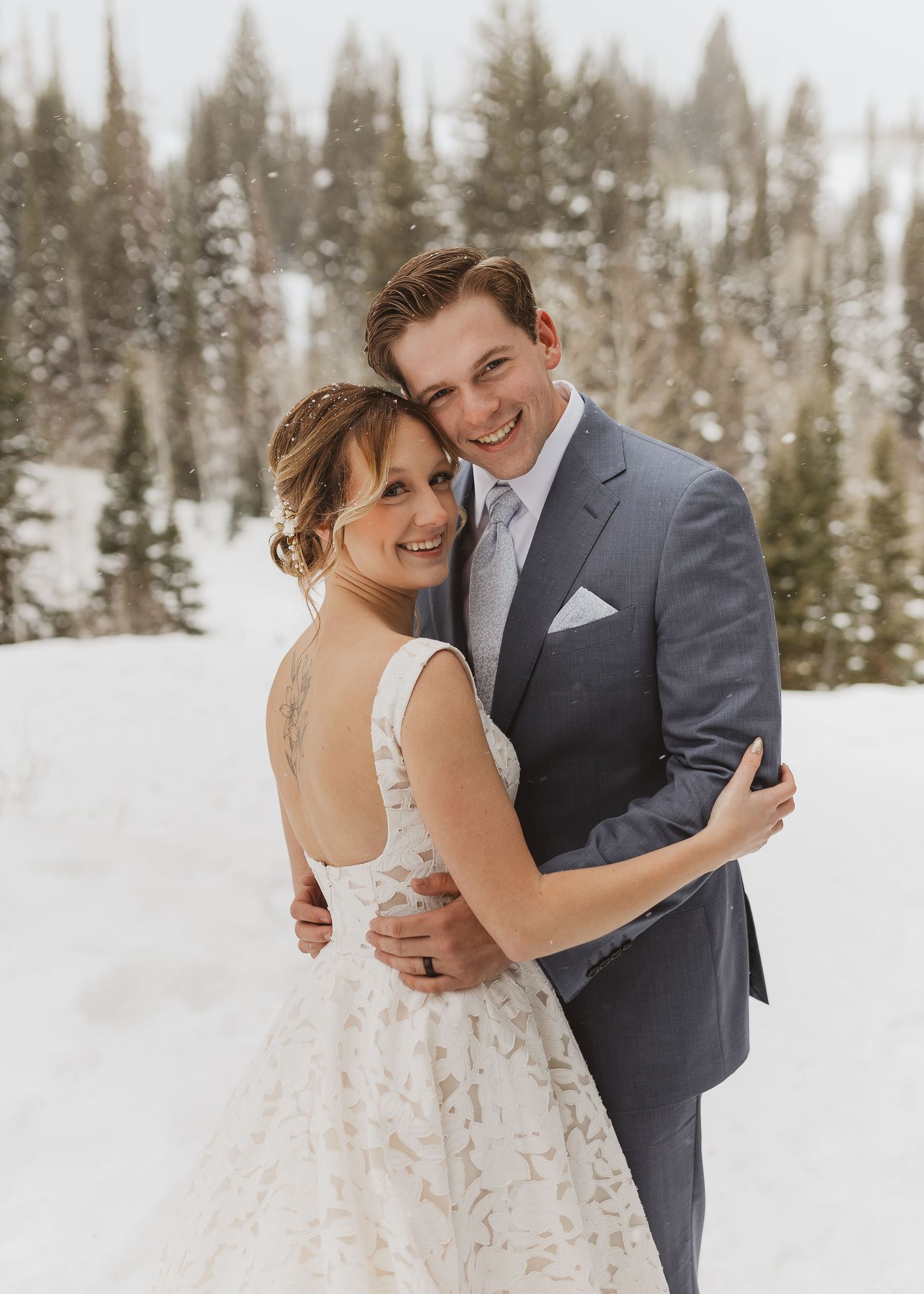 Happy couple embracing in a snowy winter wedding portrait outdoors among snow-covered trees.