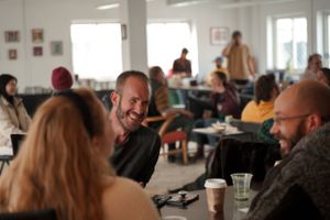 People engaged in casual conversation around tables in a bright office space.
