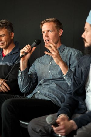 Three speakers engaged in animated discussion on a dark background stage setting.