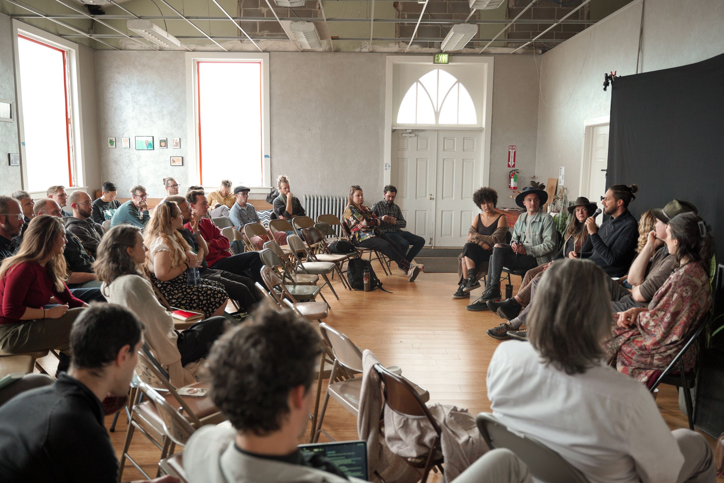 Large audience seated in folding chairs attending an indoor event in a bright room.