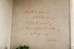Handwritten quote in brown ink on a white wall with decorative calligraphy style text.