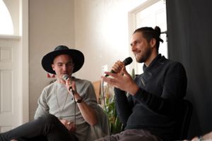 Two speakers having animated discussion with microphones in bright indoor setting.