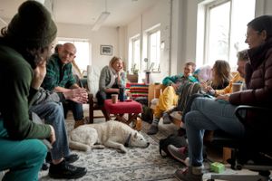 Group of people gathered in a living room setting with a dog resting on the floor.