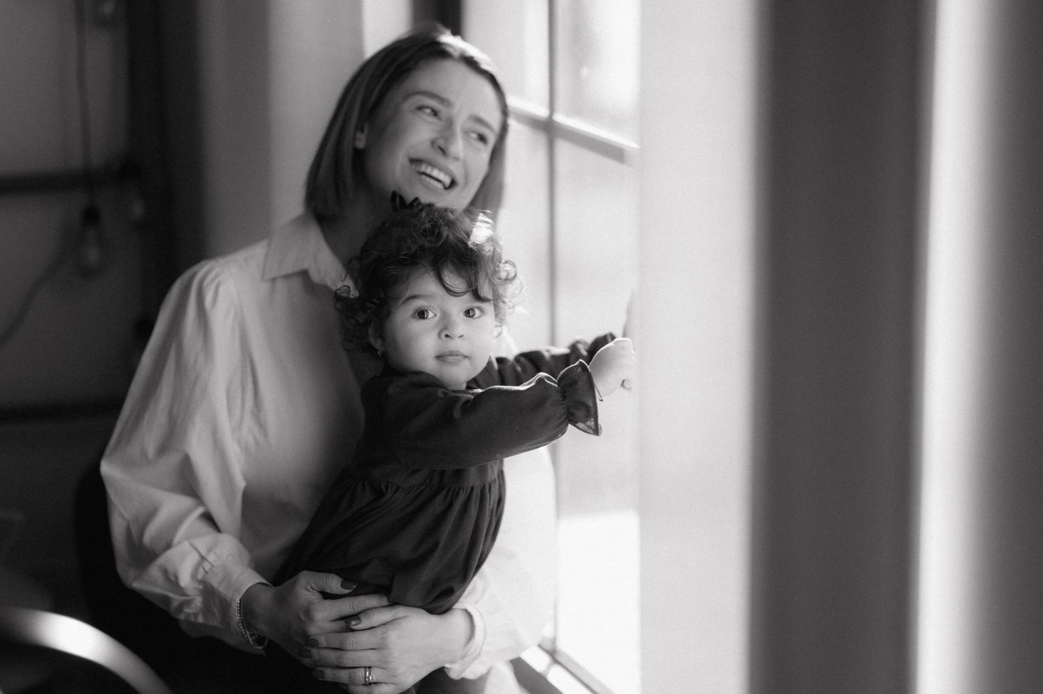 A parent and child share a tender moment by the window in this intimate black and white photograph.