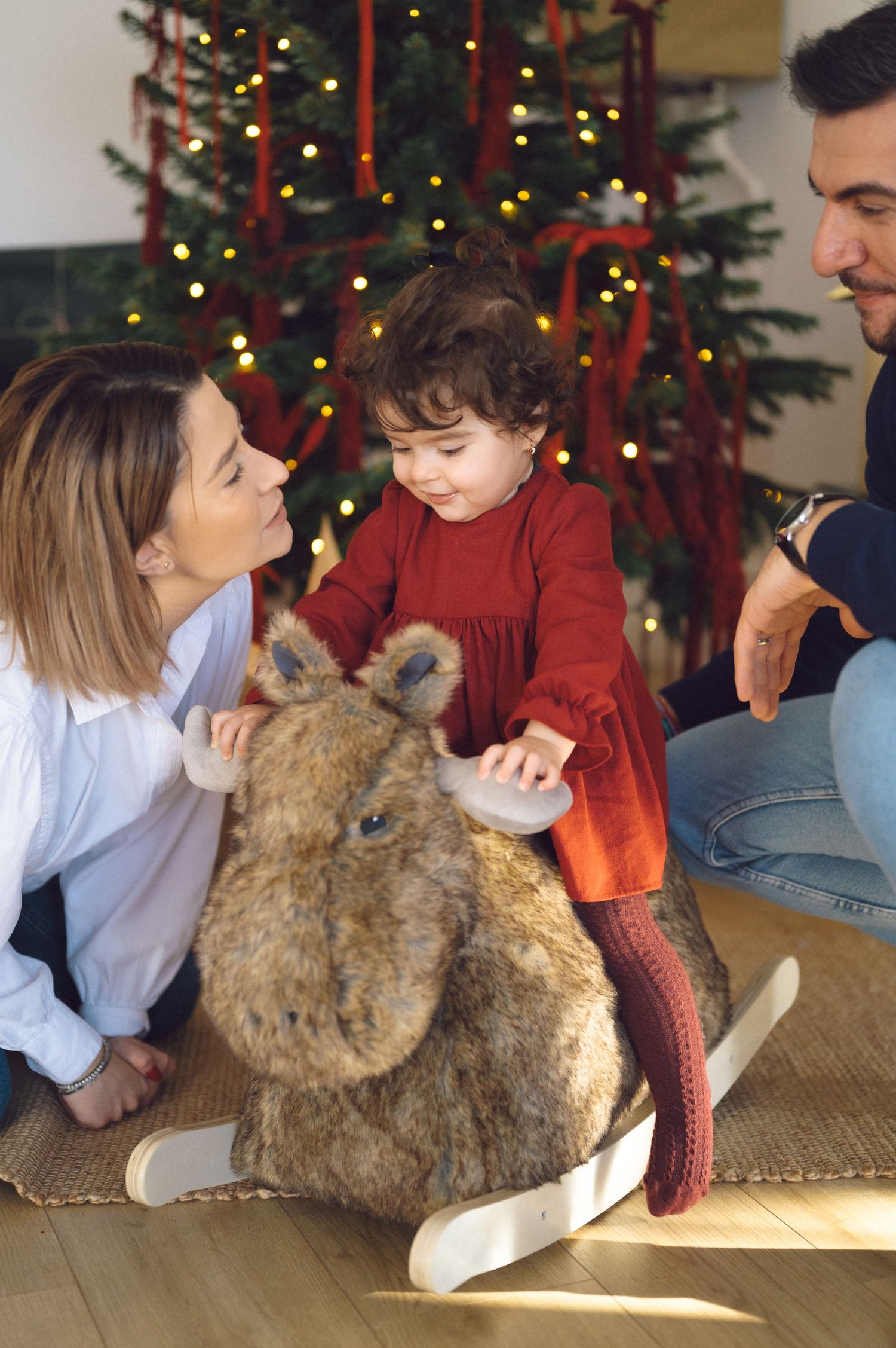 Family enjoying Christmas morning together with a plush reindeer toy in front of decorated tree.