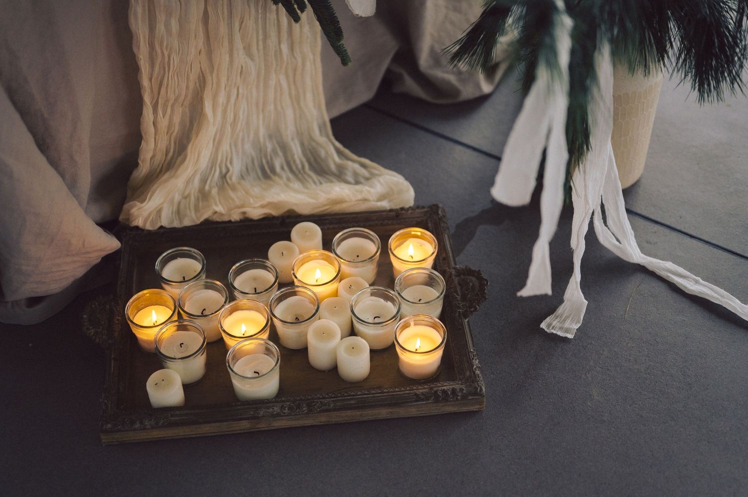 A rustic wooden tray holds glowing tea light candles in glass votives, creating a warm and intimate ambiance.