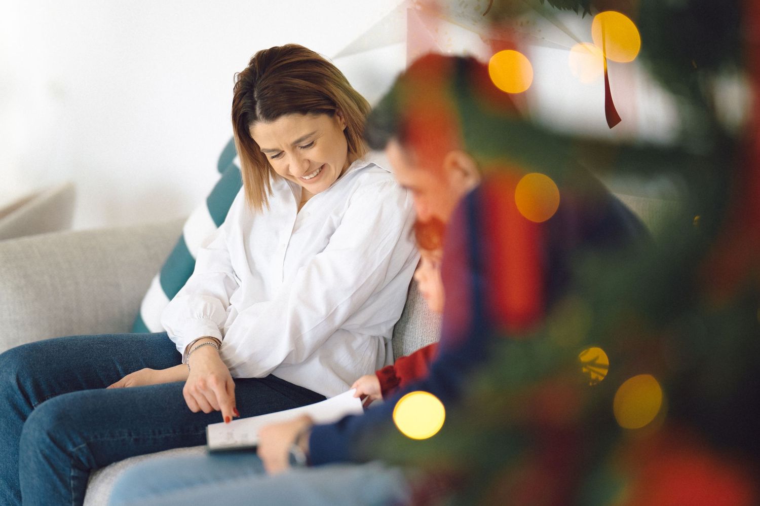 A person laughing and sorting through bright red Christmas ornaments and decorations on a wooden surface.