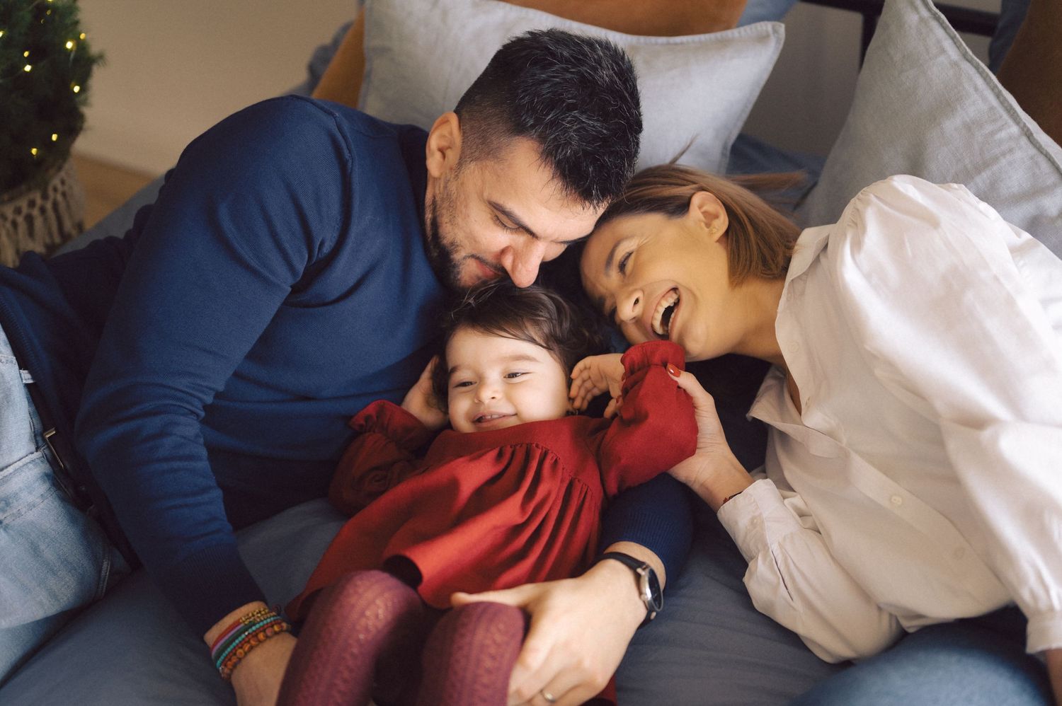 Parents cuddling with young child on couch in loving family moment.