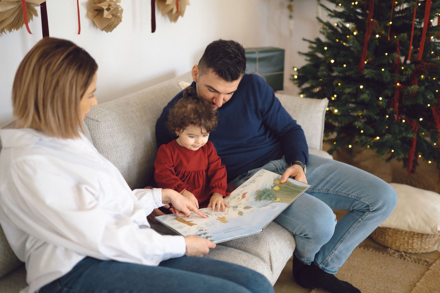 Family members sit together reading books near a decorated Christmas tree during cozy holiday time.