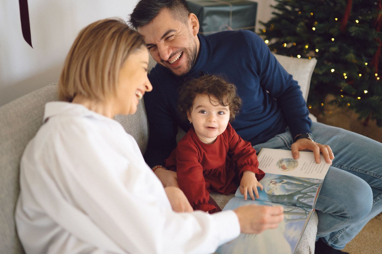 Family enjoying quality time together reading a book by the Christmas tree in cozy living room setting.