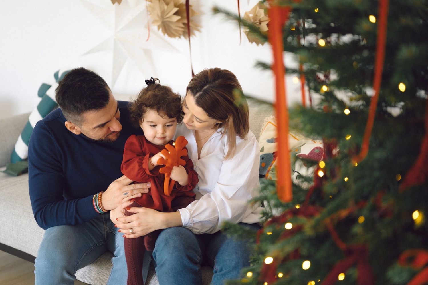 Family sits together on couch during holiday season with decorated Christmas tree in background.
