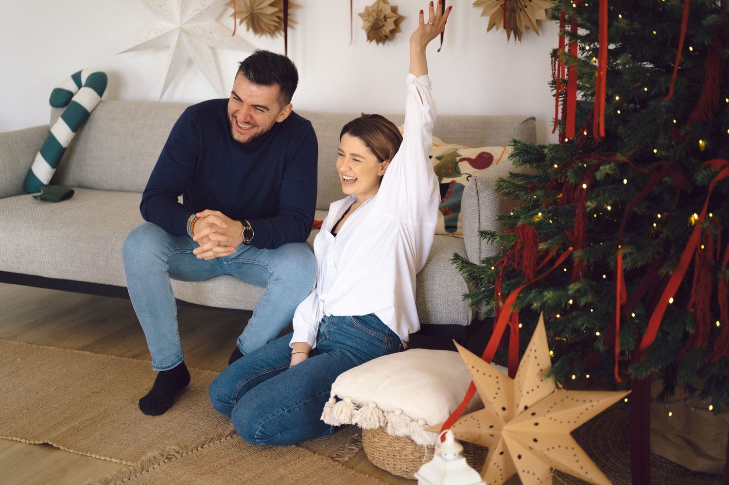 People celebrating near a holiday decorated Christmas tree with stockings and festive decor in living room.
