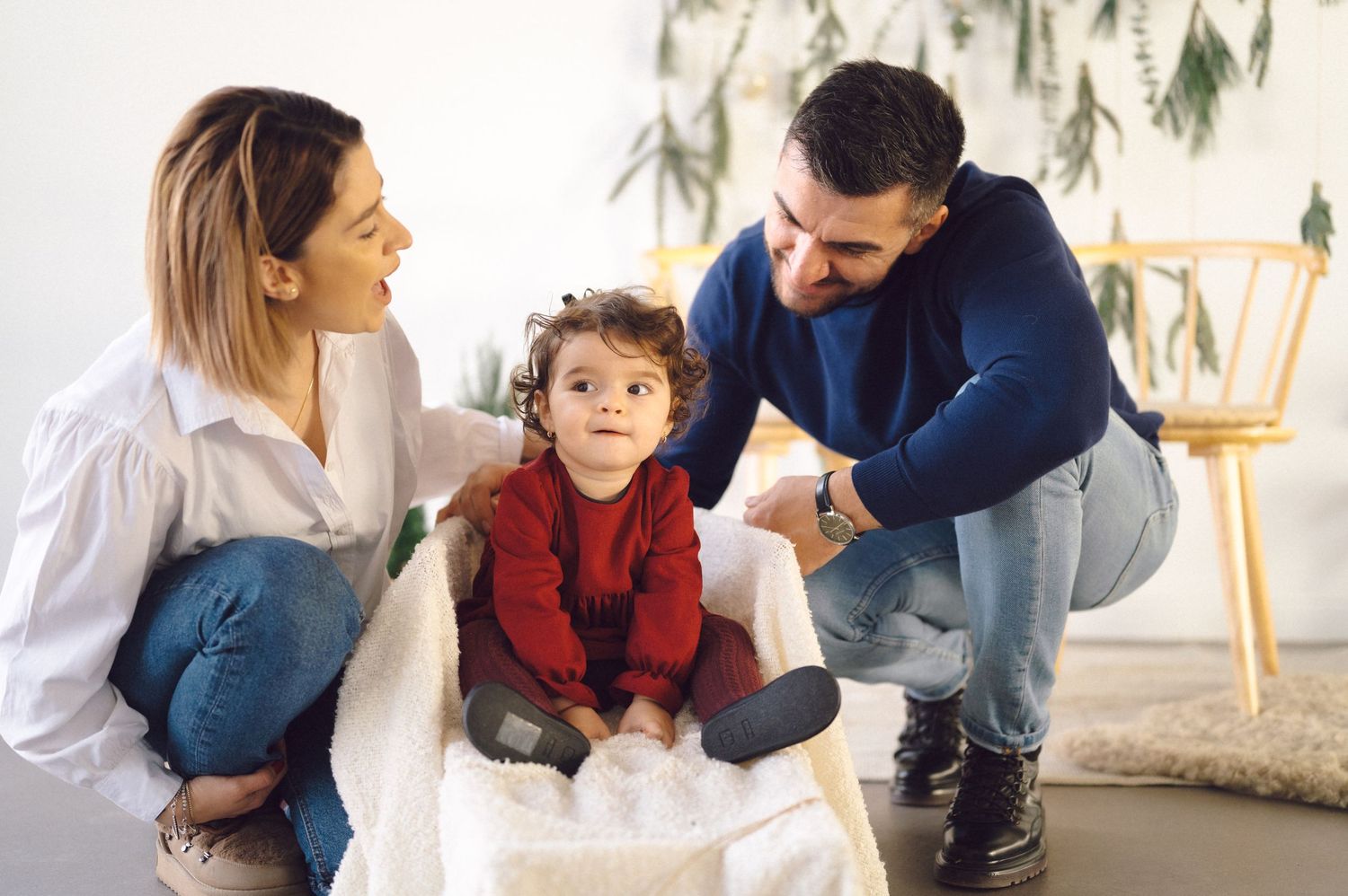 A child in a red sweater sits between two adults at home, surrounded by natural light and modern decor.