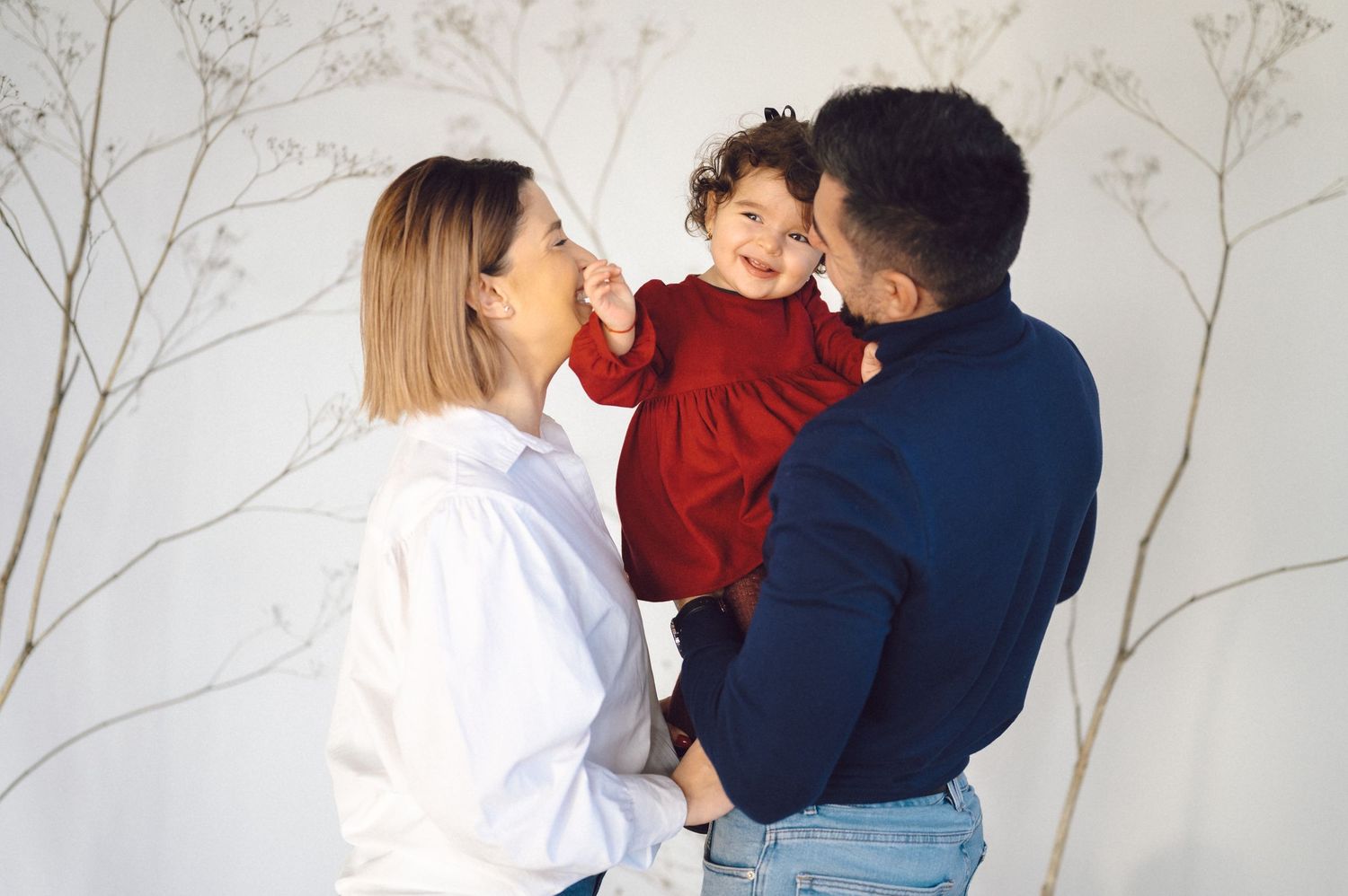 A family shares a joyful moment together against a white wall with delicate branch designs.