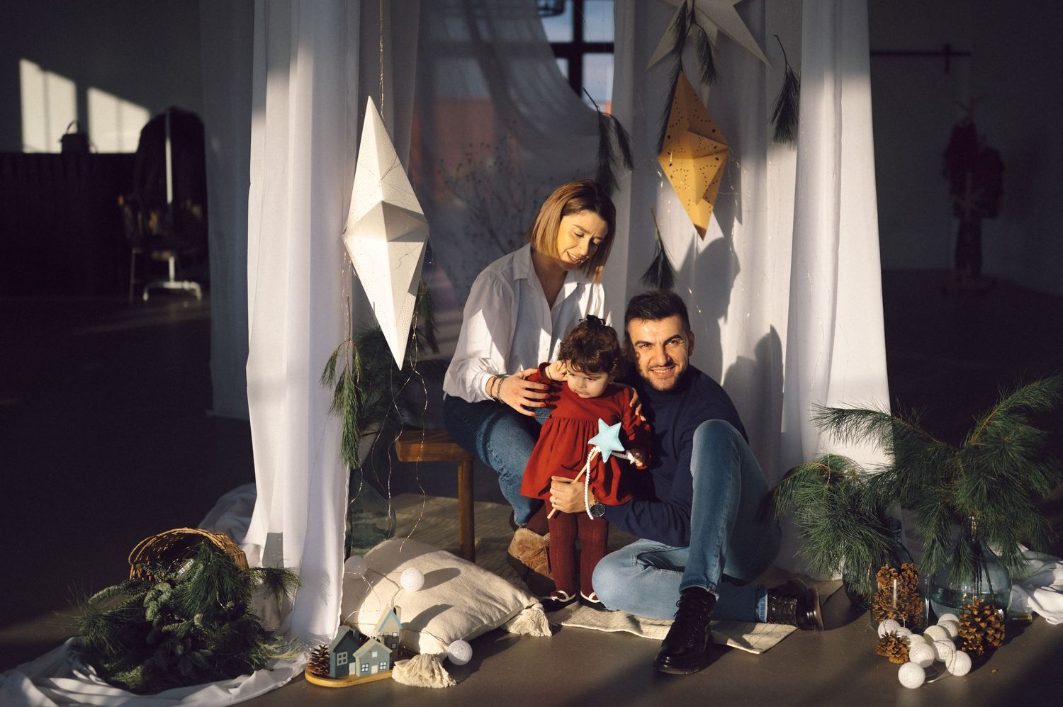 Two people sitting on floor with white curtains and decorative elements in dark interior lit by dramatic lighting.