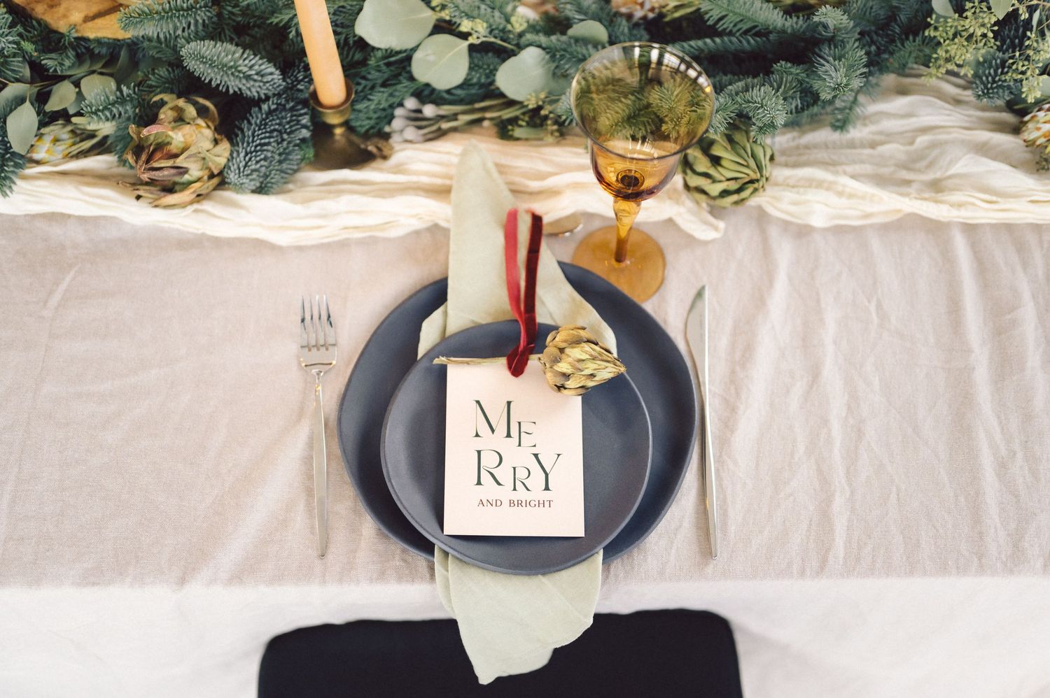 Close-up view of elegant white linen wedding table settings with black plates and fresh eucalyptus garland decorations.