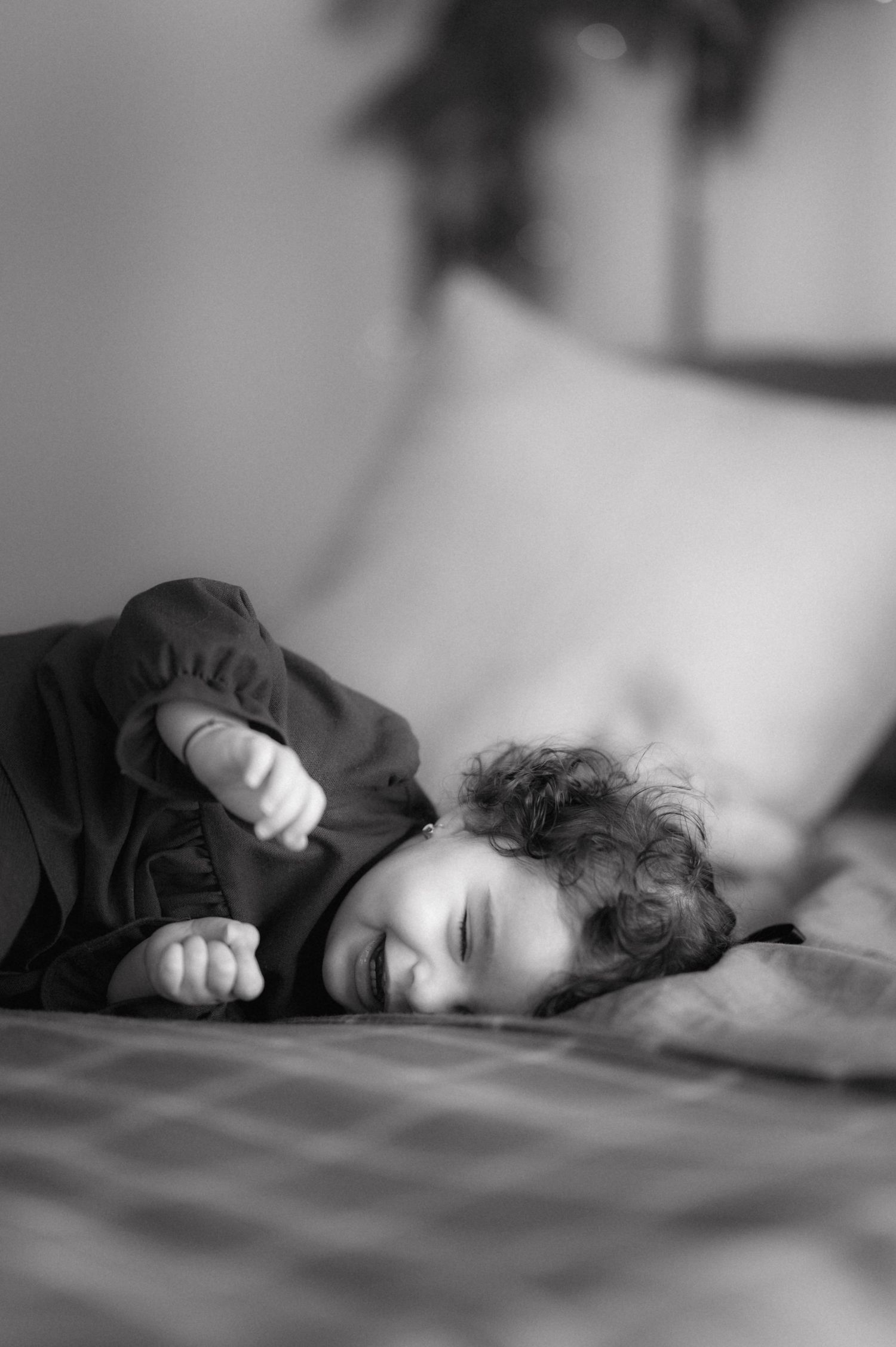 Black and white image showing a child sleeping peacefully curled up in soft bedding.