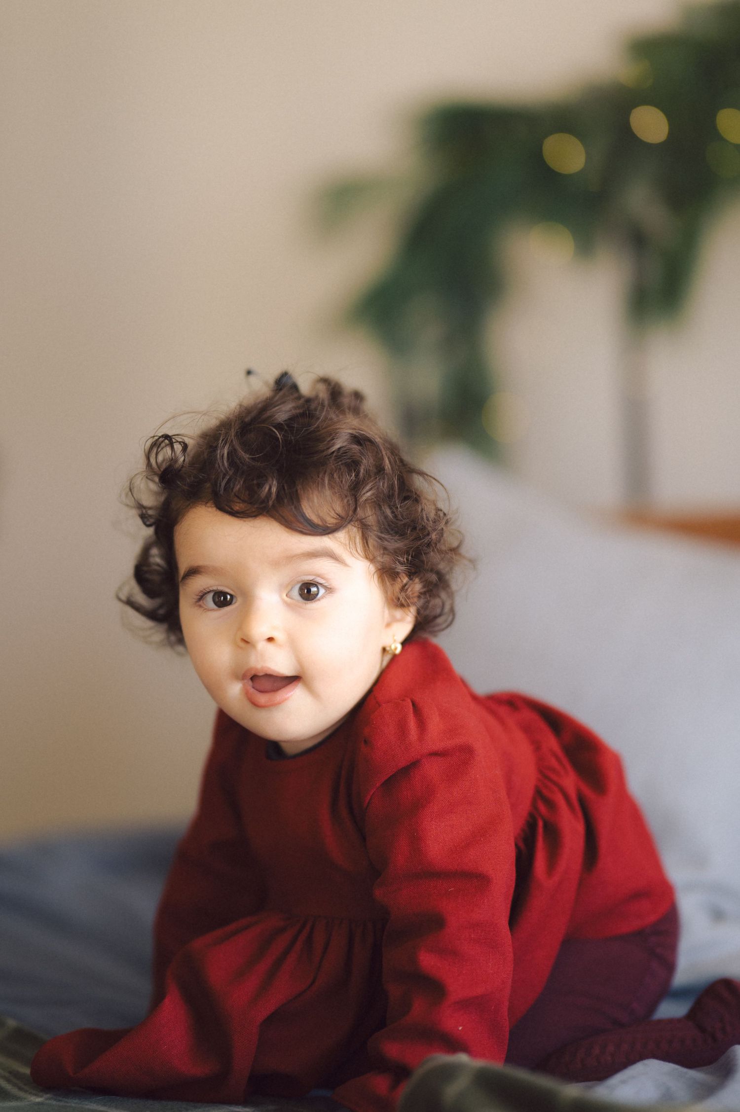 Young child wearing a red sweater lying on stomach on a grey surface with indoor greenery visible in background.