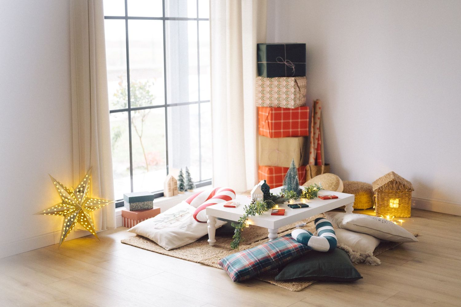Cozy reading nook by window with illuminated star lights, blankets, and scattered books on hardwood floor.