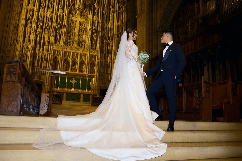 Elegant wedding couple stands on church steps with bride's dramatic cathedral train in full view.