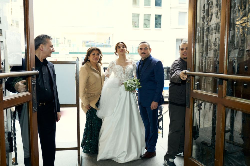 Wedding party gathers at church entrance in formal attire with bride in classic white gown.