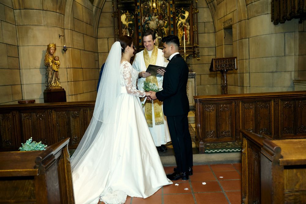 Wedding ceremony takes place in historic church interior with wooden paneling and statuary.