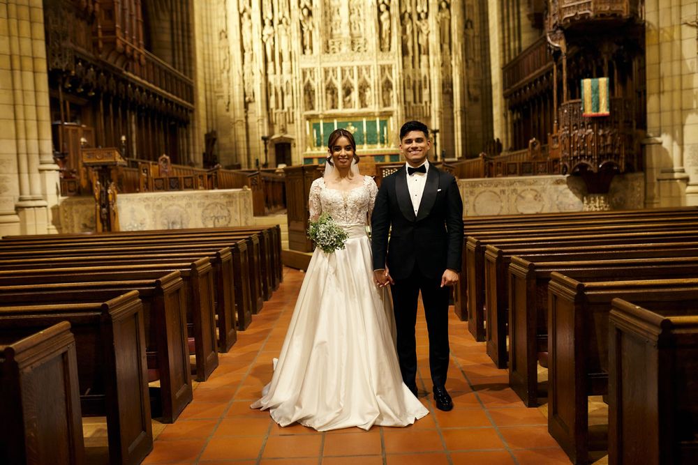 Bride and groom walk down church aisle with Gothic architecture and wooden pews visible.