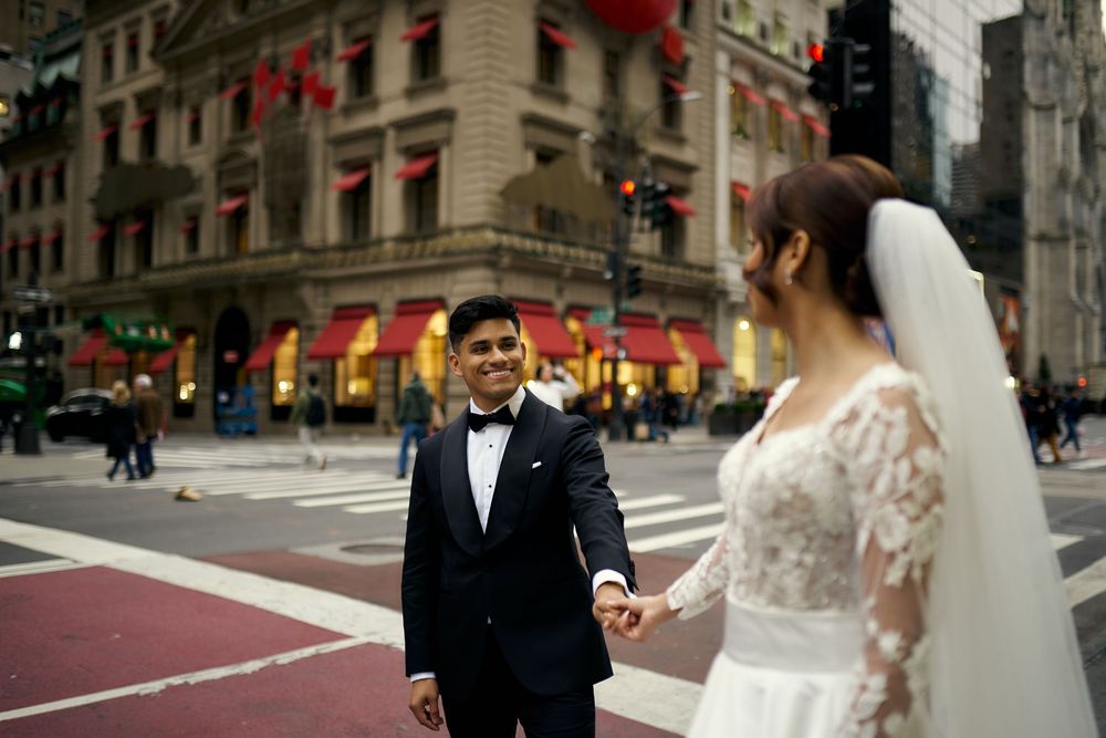 Newlyweds share moment on city street with classic architecture in background.