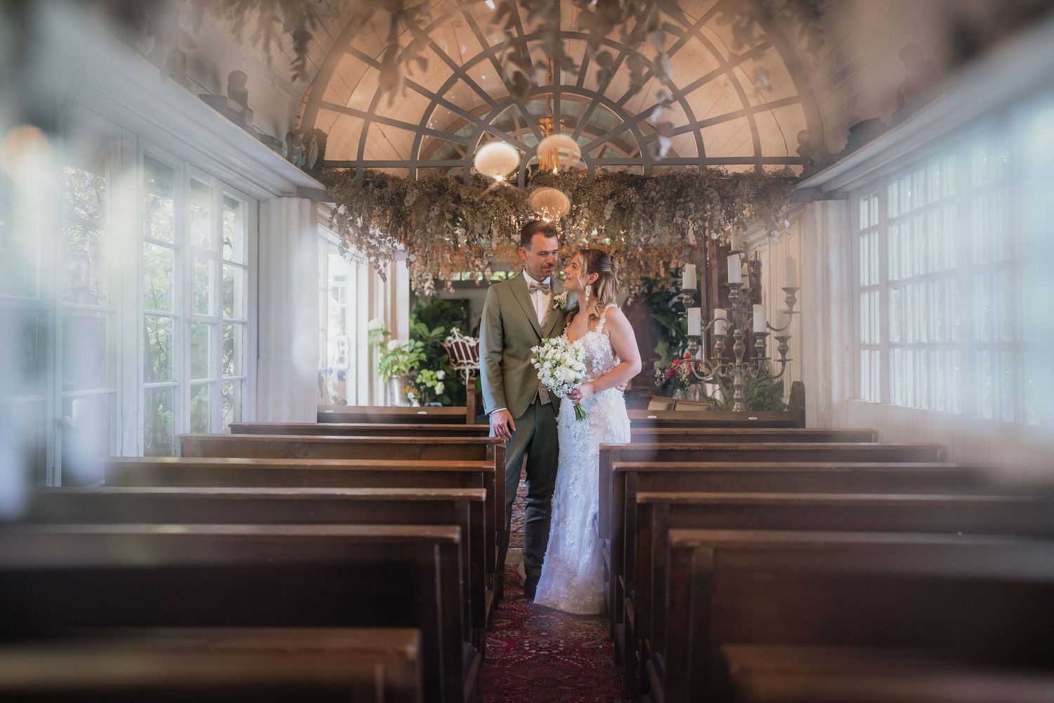 Wedding couple stands in beautiful chapel with ornate ceiling and wooden pews.