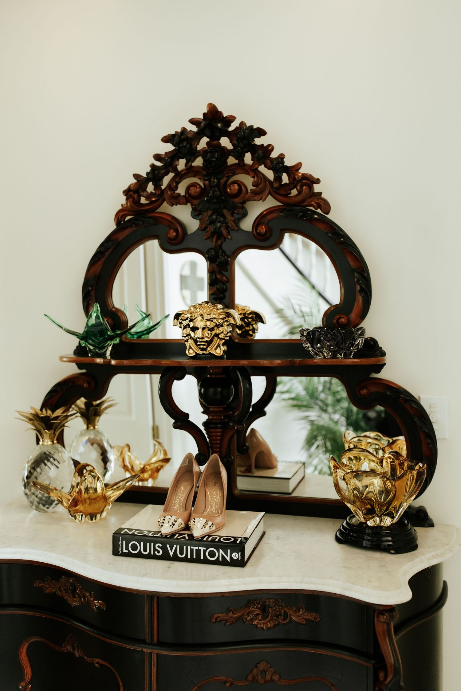 Ornate dark wood display shelf with decorative Louis Vuitton books and gold accents against a white wall.