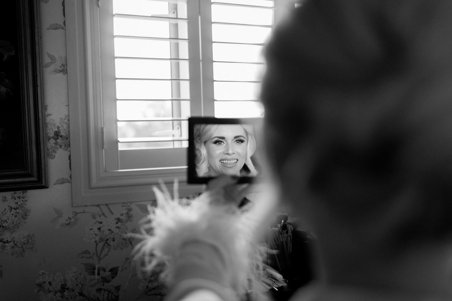 A black and white photograph shows a reflection in a mirror with a fluffy white cat in the foreground.