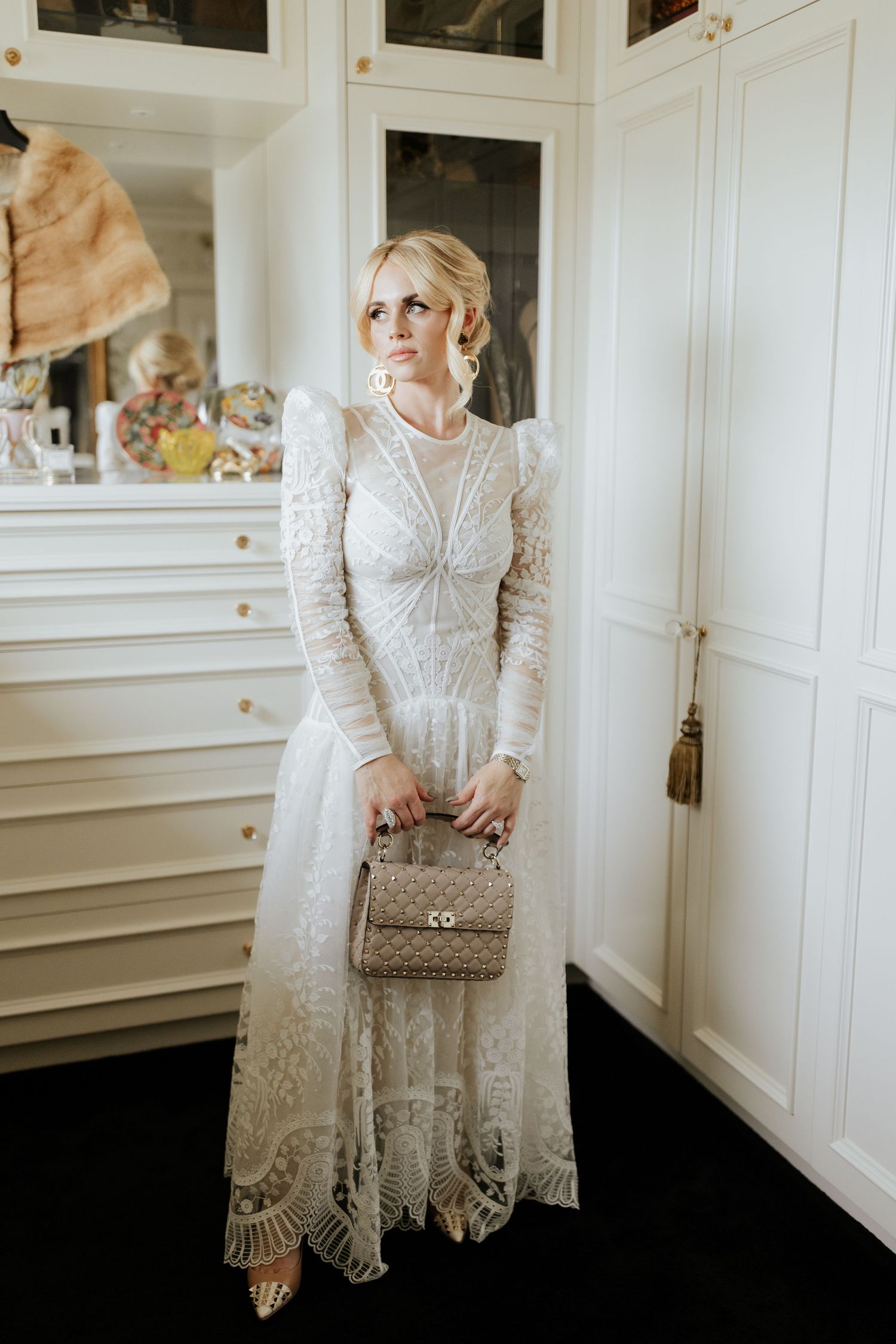 Elegant vintage-inspired lace wedding dress with long sleeves and a classic Chanel quilted bag.