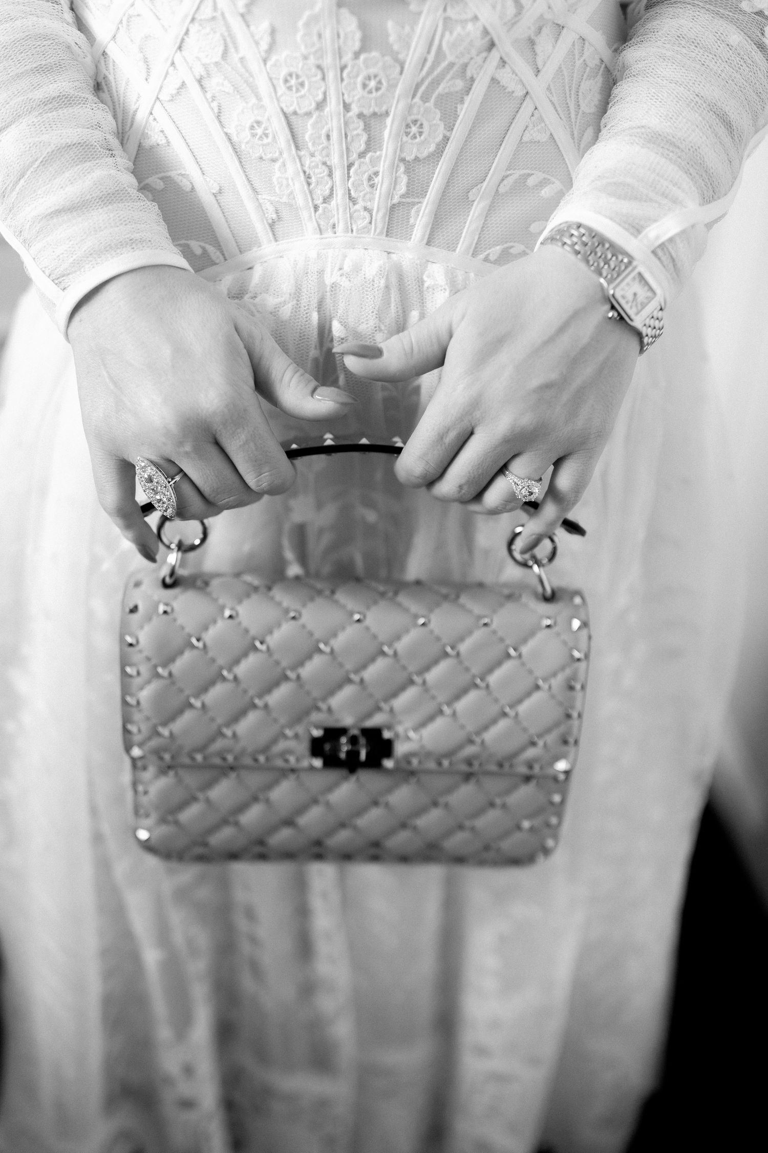 Close-up view of hands holding a metallic quilted Chanel handbag with a white lace dress.