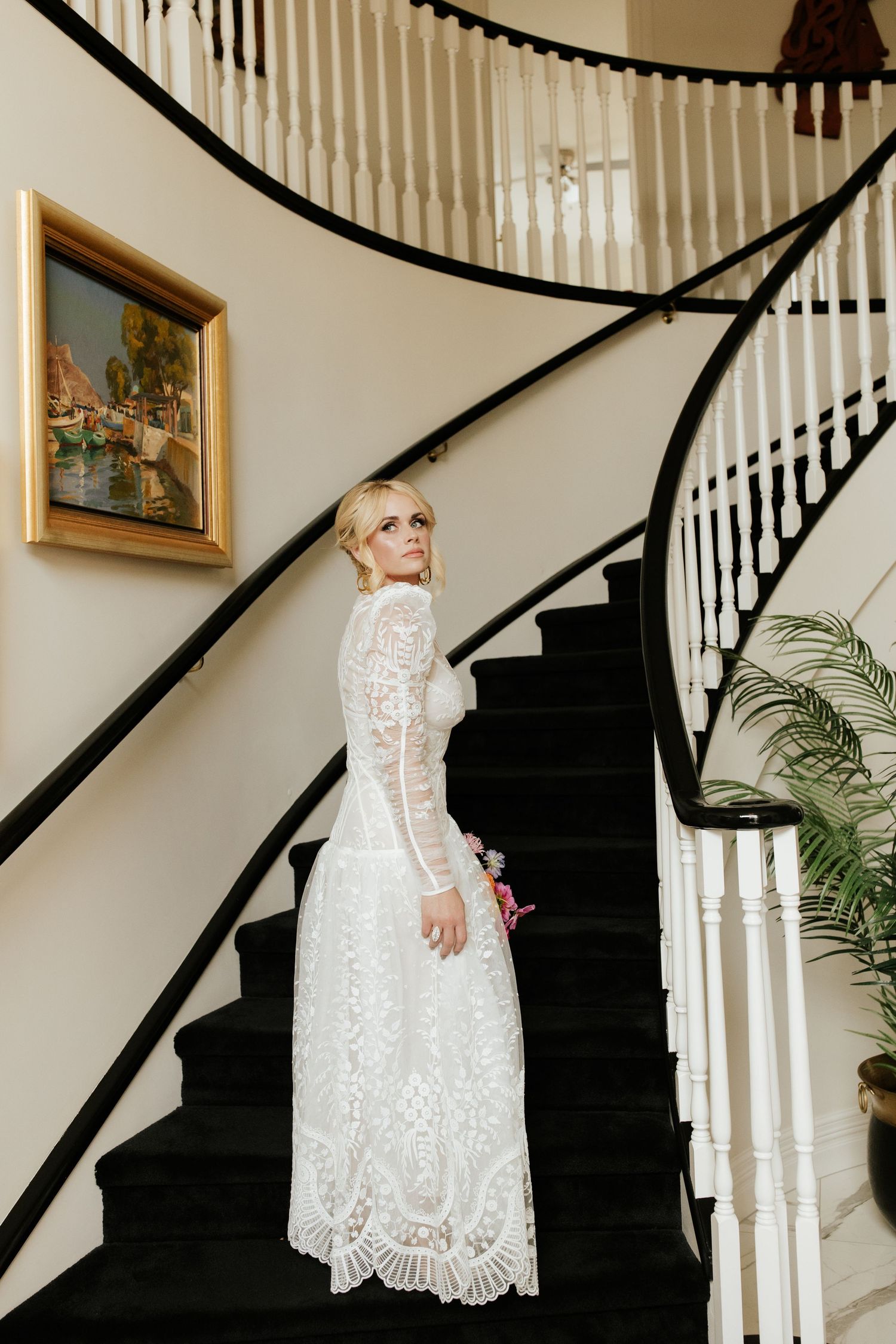 Elegant lace wedding dress with long sleeves photographed on a curved staircase with black carpet.