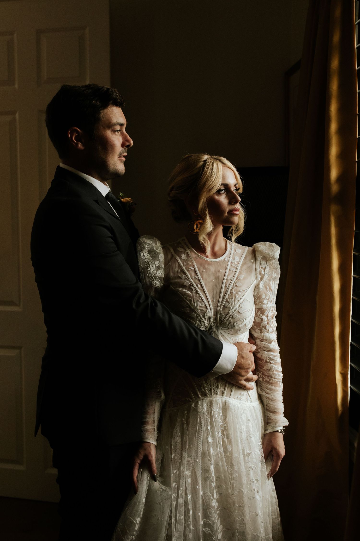 Dramatic window-lit portrait of a couple in wedding attire creating an intimate moment.