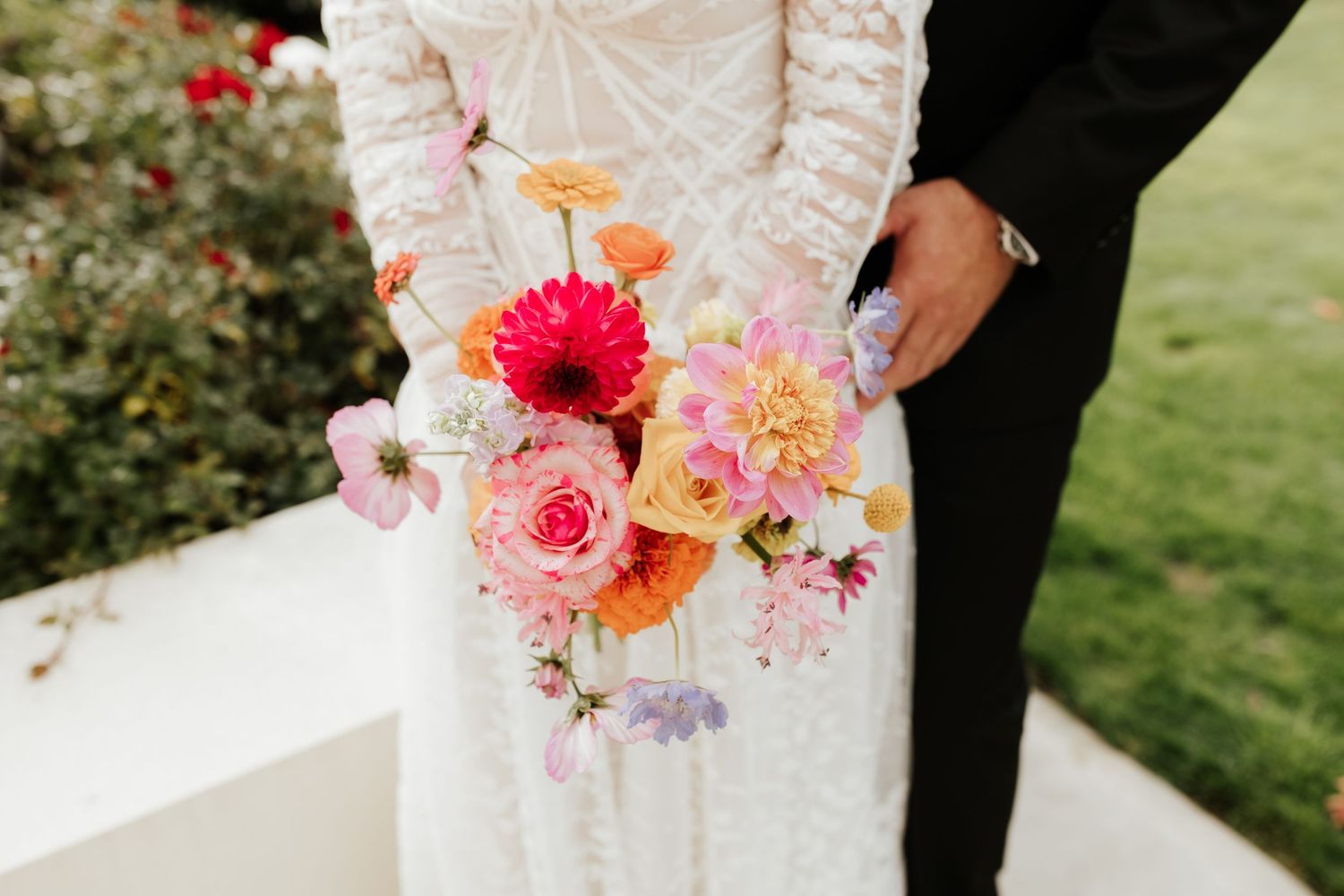 Pink and coral floral bouquet details shown against white lace wedding dress.