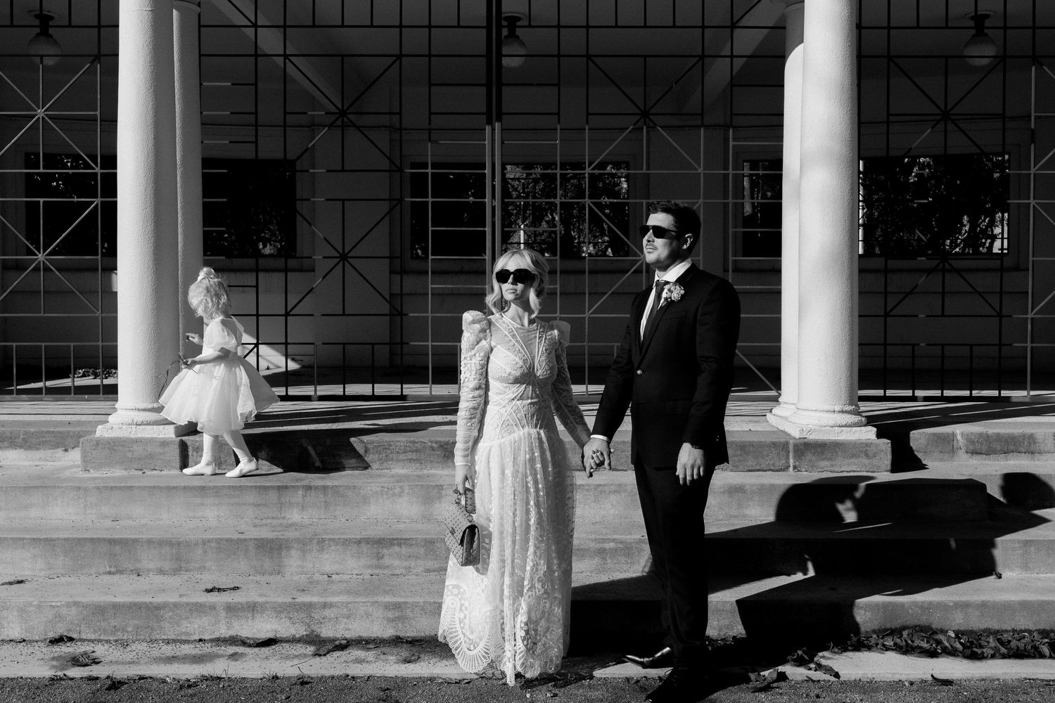 Wedding party standing between white columns at elegant venue with geometric window patterns.