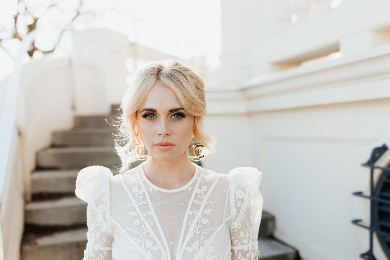 Elegant lace wedding dress with puff sleeves photographed outdoors against a white building.