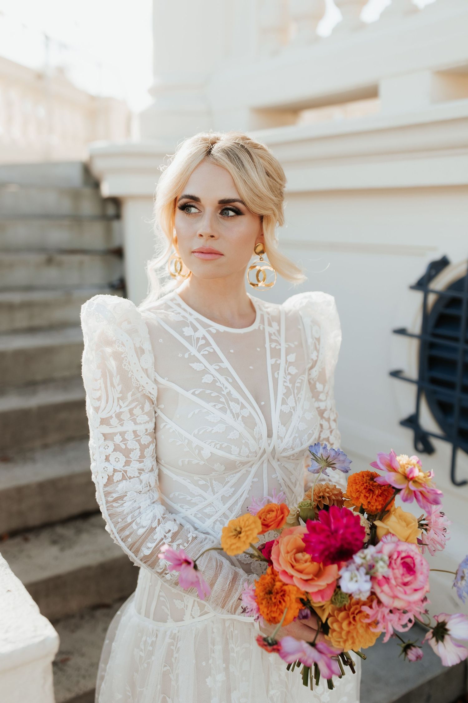 Elegant bridal portrait on steps with vibrant colorful wedding bouquet against white architecture.