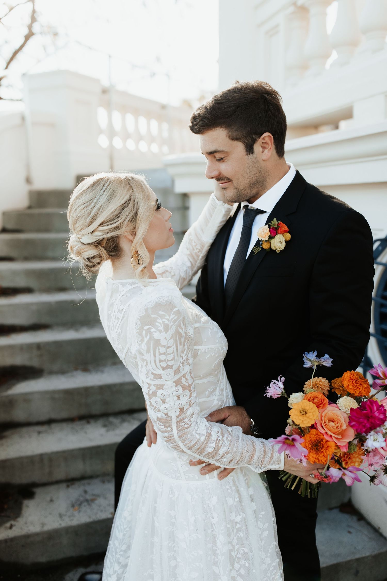 A romantic wedding portrait on stairs showing a couple in classic attire with a colorful floral bouquet.