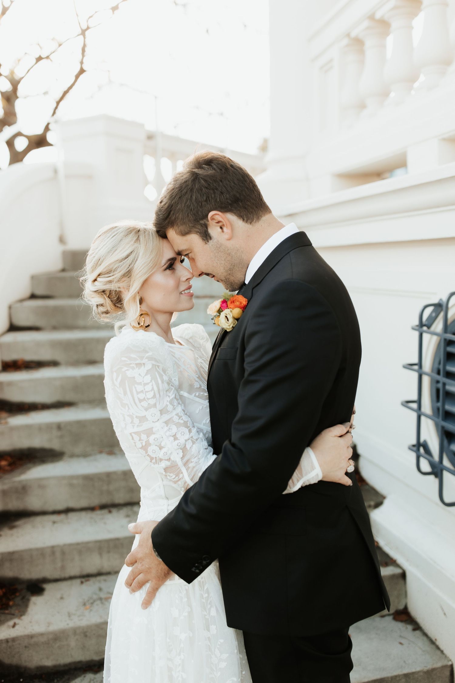 A romantic wedding moment captured with the couple embracing on white steps in black and white formal attire.