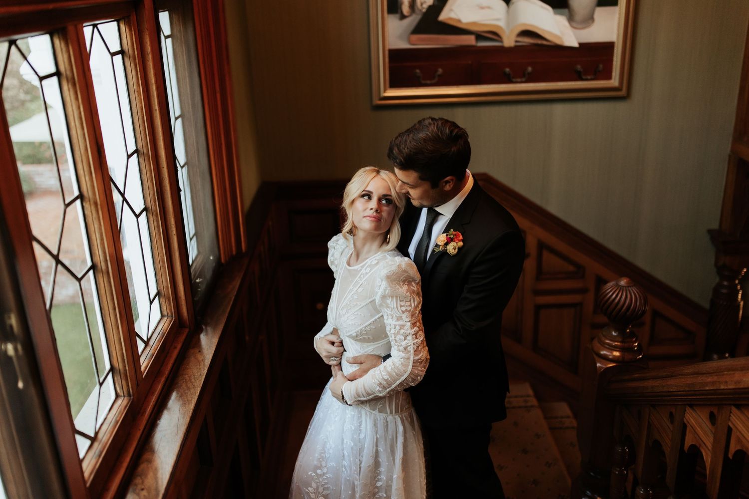 An intimate wedding scene showing a couple sharing a tender moment in front of sunlit windows.