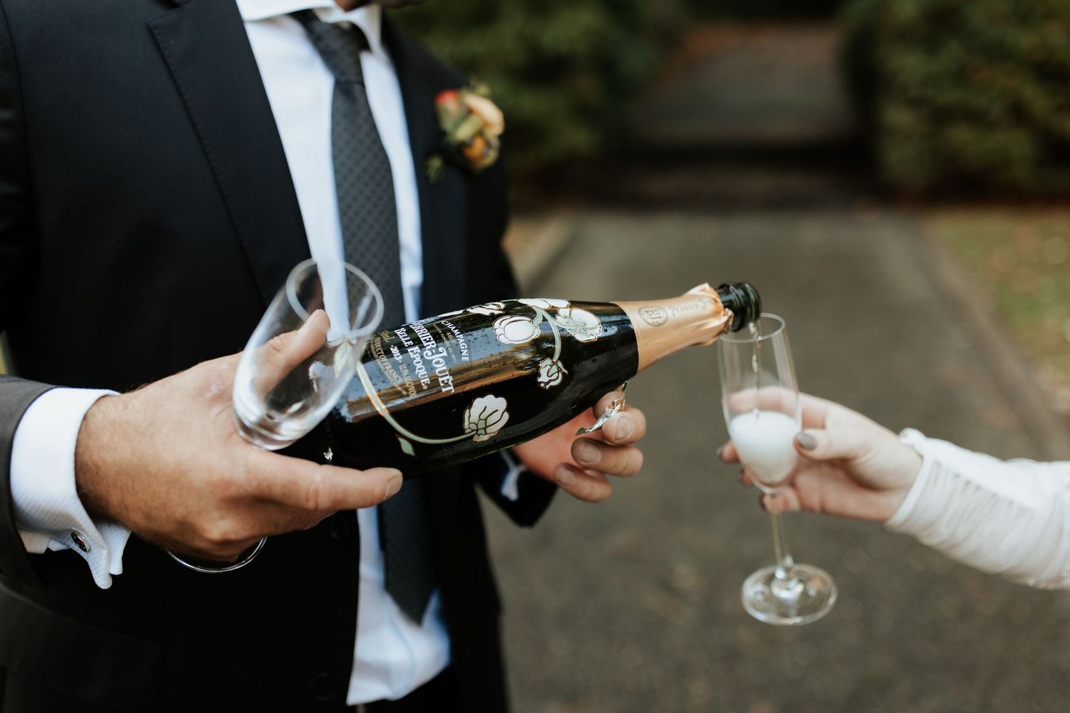Two hands in formal attire clink champagne glasses together in a celebratory toast.
