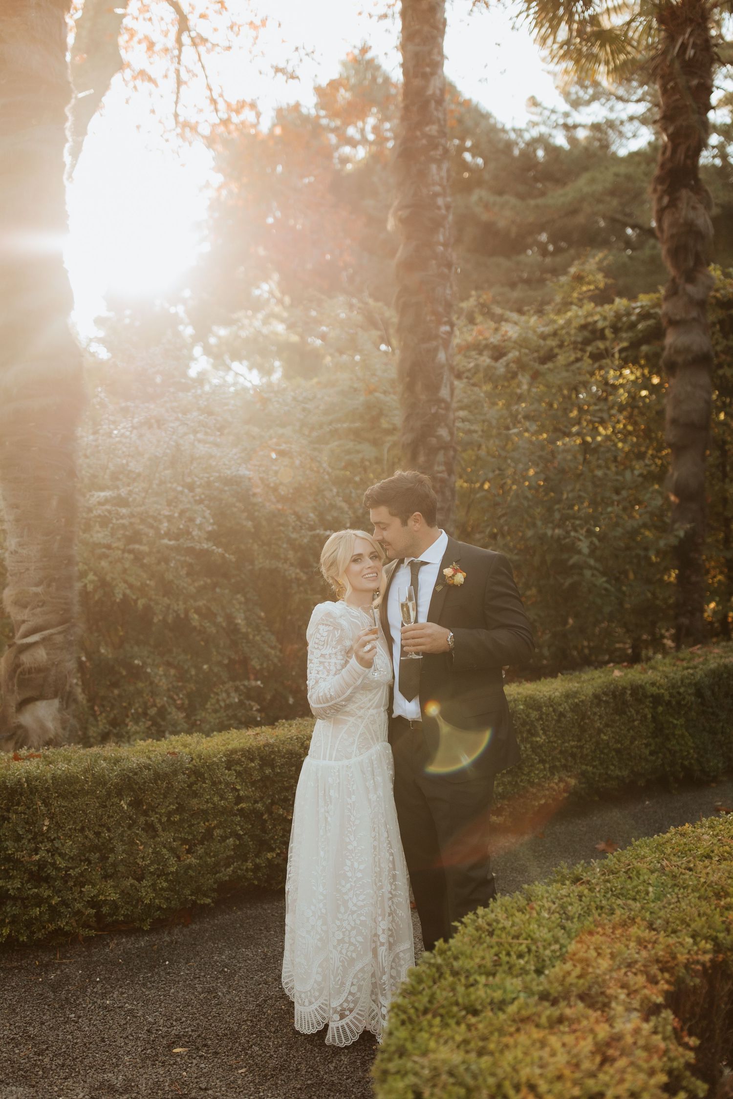 Couple dancing together in a beautiful garden setting during golden hour with warm sunlit trees in background.