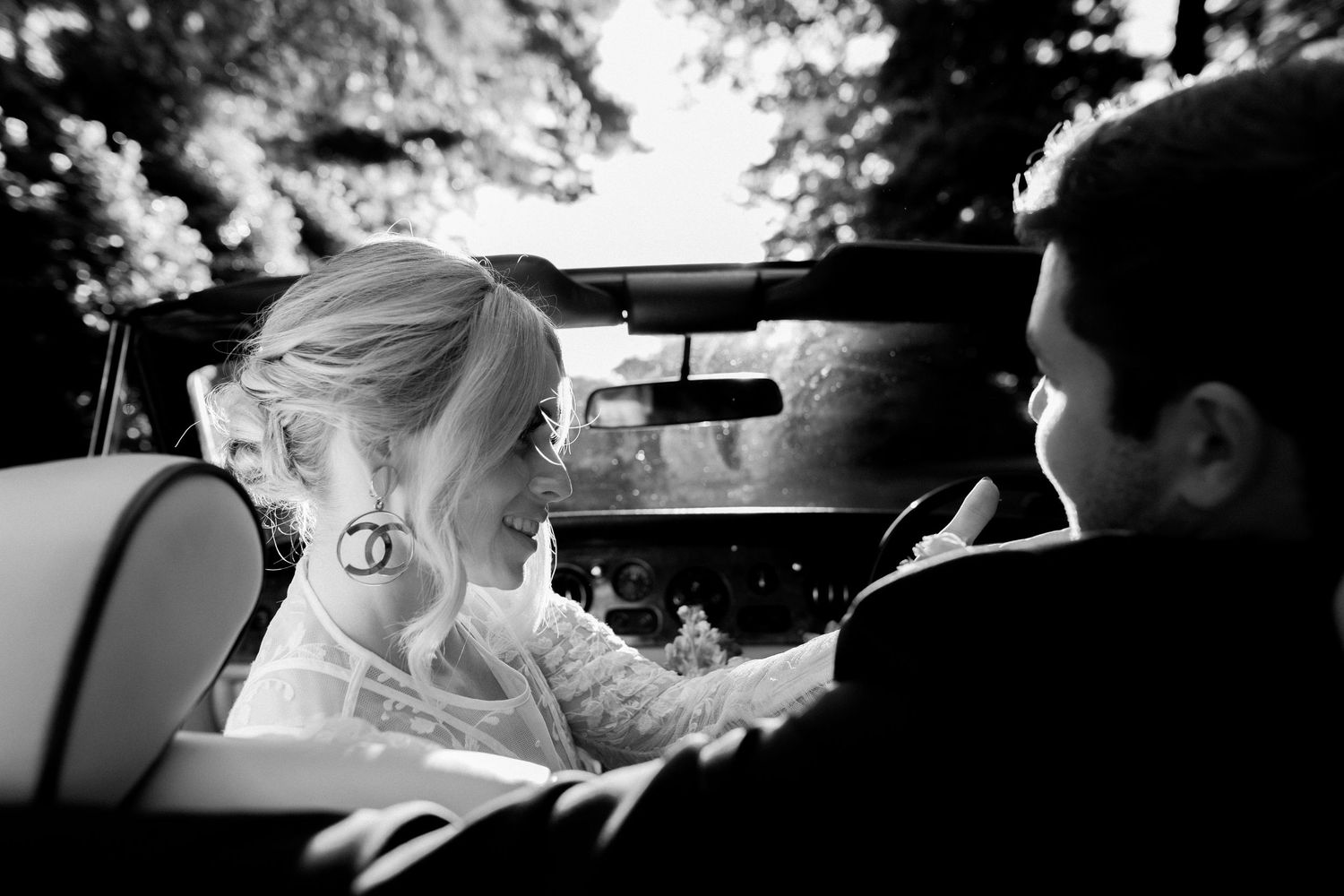 A black and white photograph showing two people sitting in a convertible car looking at each other.