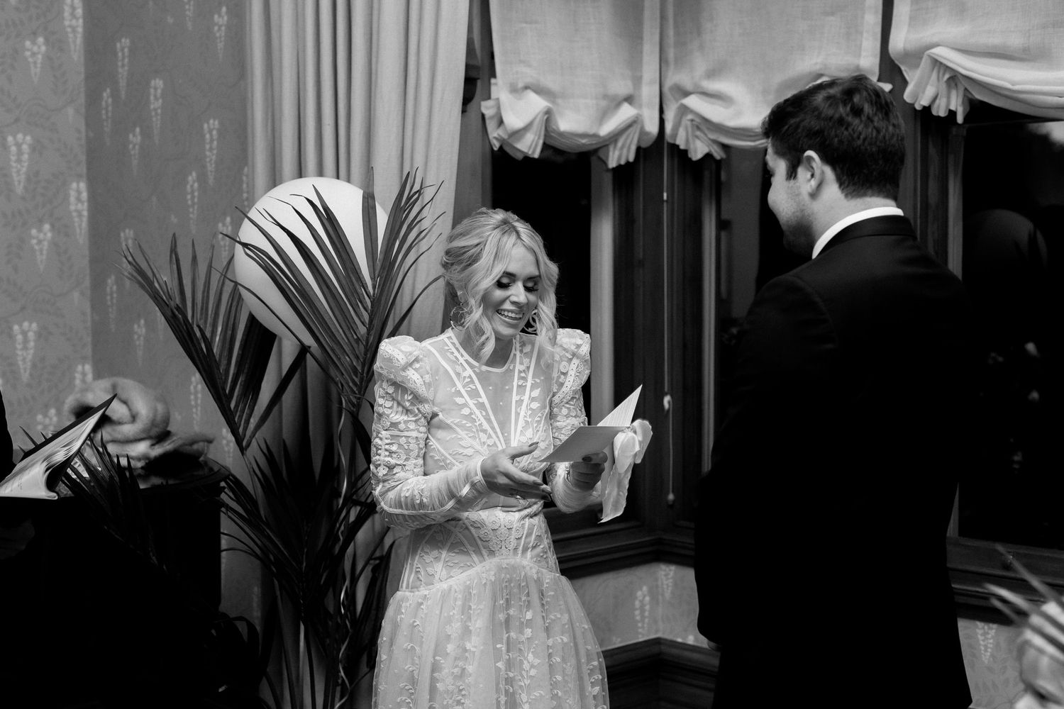 A black and white photograph shows a well-dressed couple sharing a joyful moment together at an event.